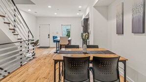 A modern dining area with a wooden table, black chairs, and a staircase with metal railings.