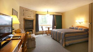 A hotel room with a bed, a desk with a television, a fireplace, a dining area, and a window. - Beautiful Lakefront Inn Suites (Parry Sound)