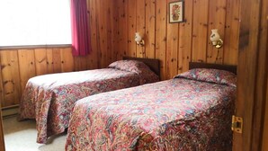 A room with two single beds with floral bedding, wooden walls, and a window with a curtain.