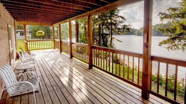A covered deck with wooden railings, a table, and two chairs.