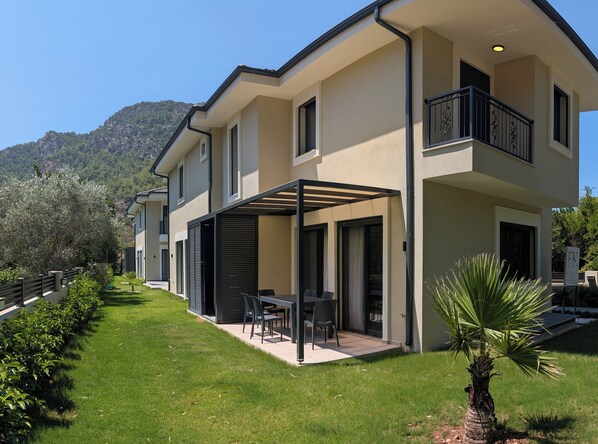 A modern two-story house with a covered patio, a balcony, and a well-maintained lawn.