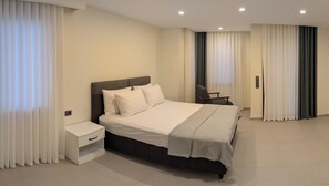 A modern hotel room with a large bed, a bedside table, and a chair.
