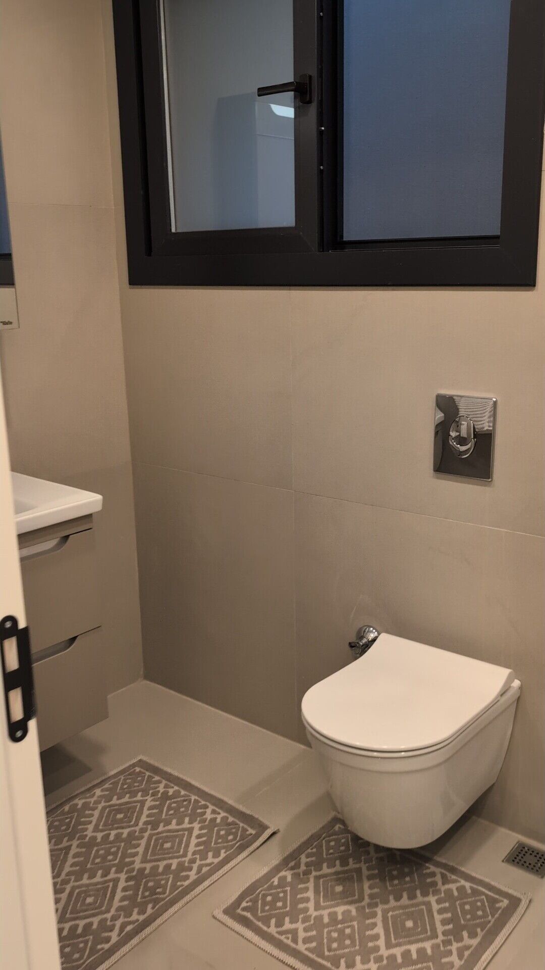 Un baño pequeño y limpio con inodoro, lavamanos y ventana sobre el inodoro.