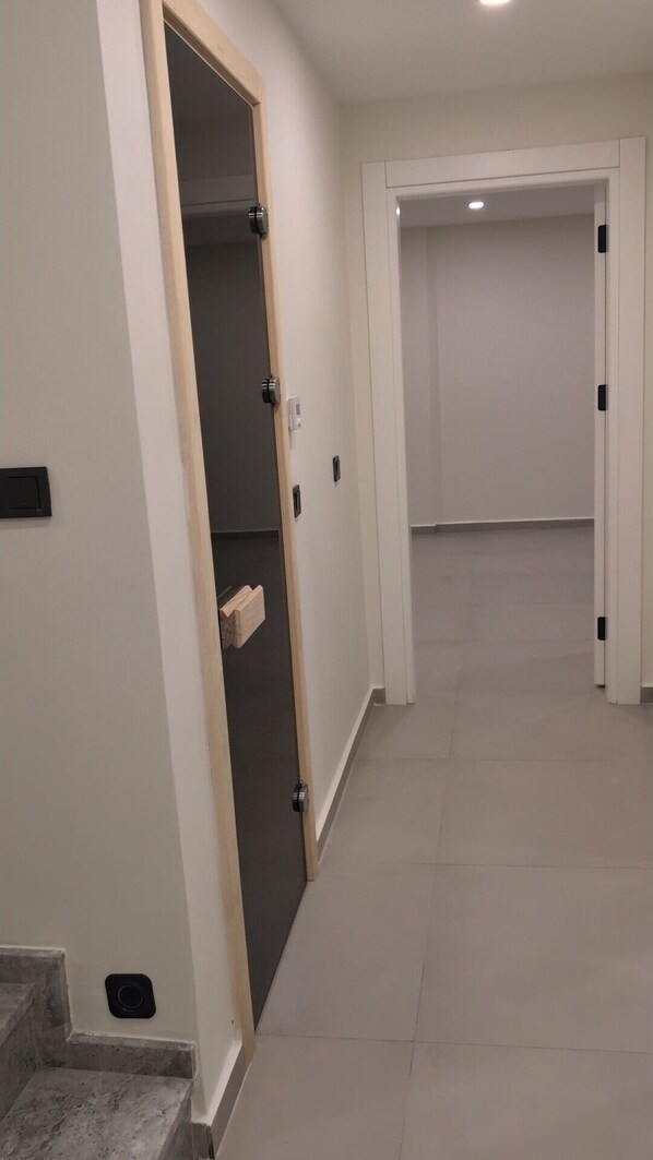 Un pasillo con una puerta que da a una habitación, una escalera y una pared lisa con un interruptor de luz.
