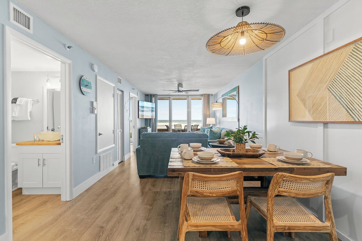 Un coin repas avec une table en bois dressée pour quatre personnes, entourée de chaises en osier.