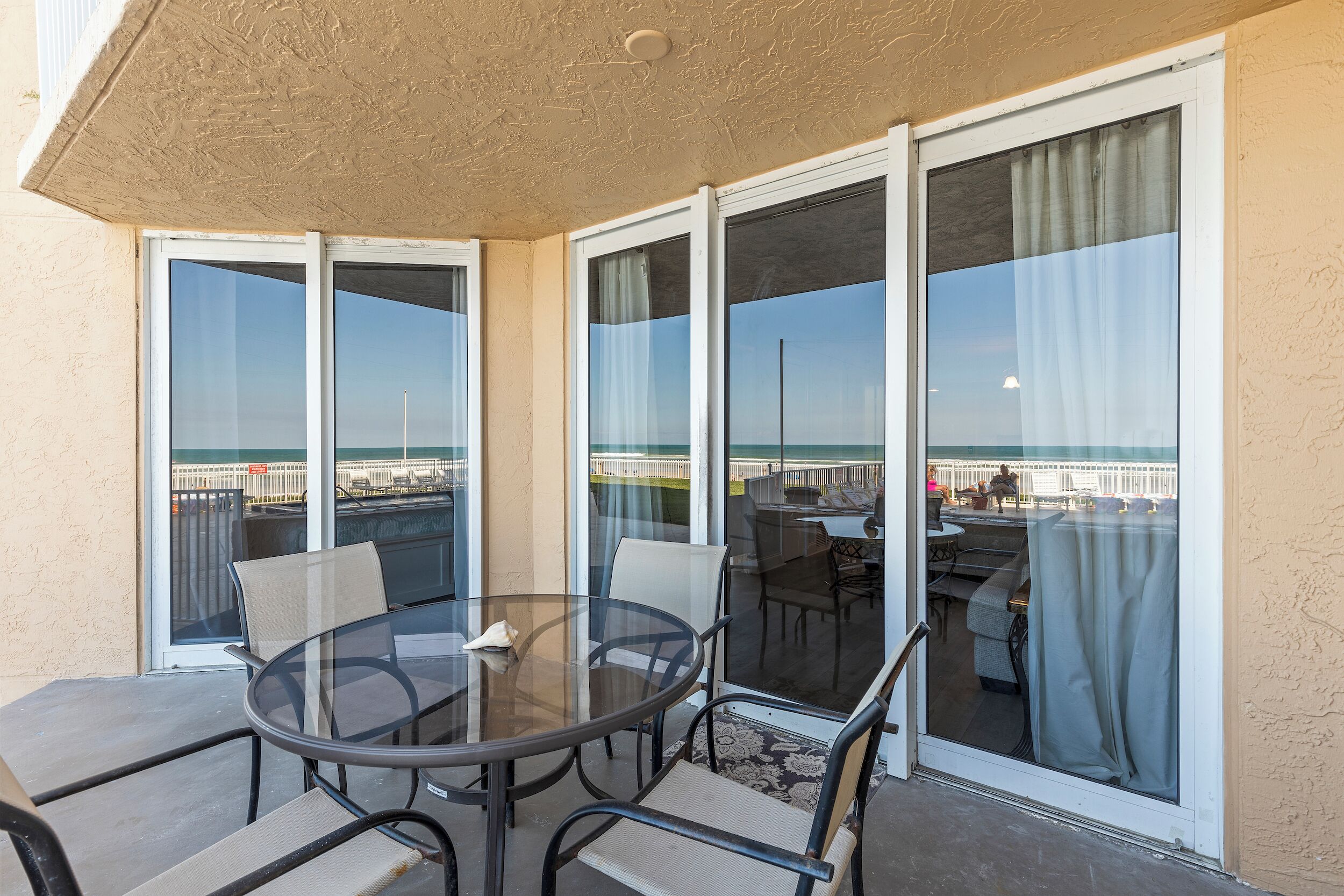 Uma varanda com mesa e cadeiras de vidro, amplas portas de correr e vista para a praia e o horizonte da cidade.