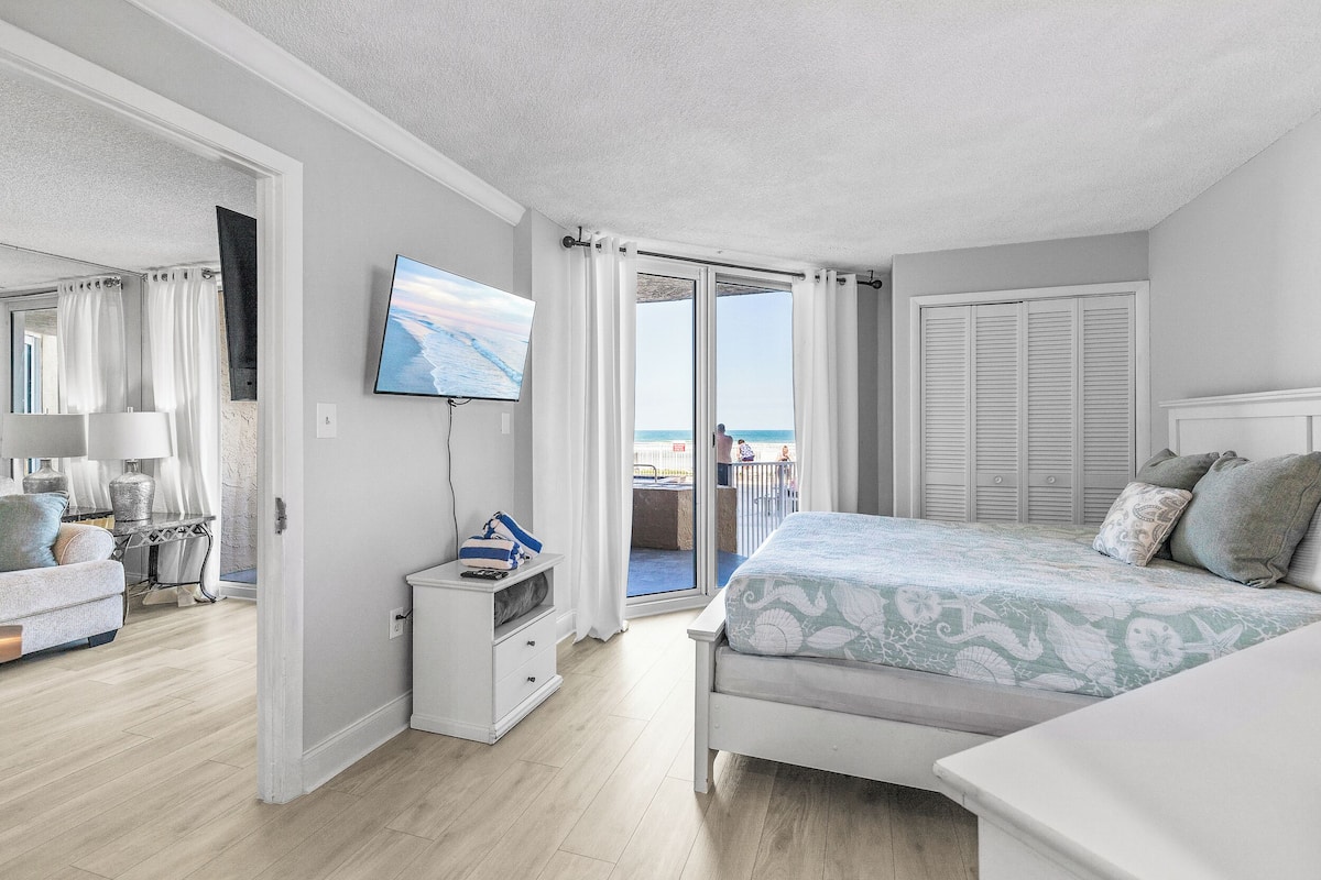 Une chambre à coucher avec un lit, une télévision, une commode et un balcon donnant sur la mer.