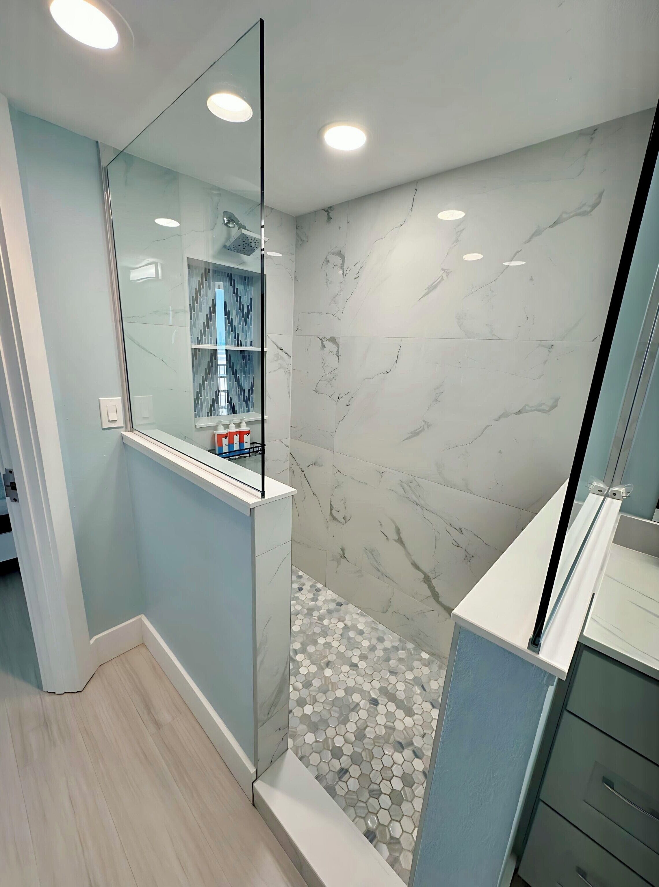 Um banheiro moderno com box de vidro, paredes de mármore e piso de azulejos hexagonais.