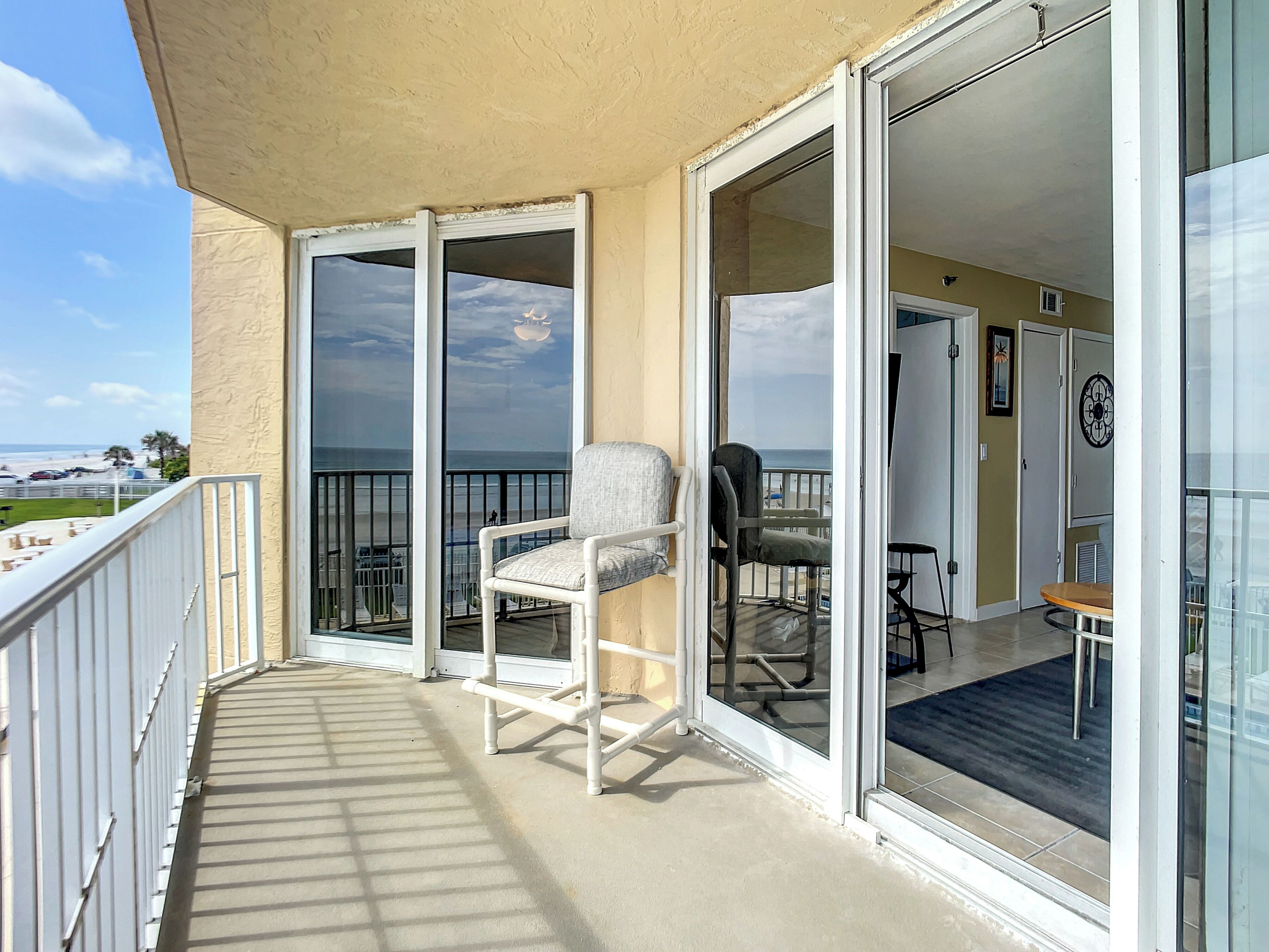 A balcony with a chair and a table, a sliding glass door, and a view of the beach.