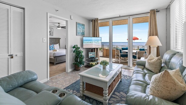 Un salon avec un canapé, une table basse et un téléviseur. Il y a un balcon avec vue sur la mer.