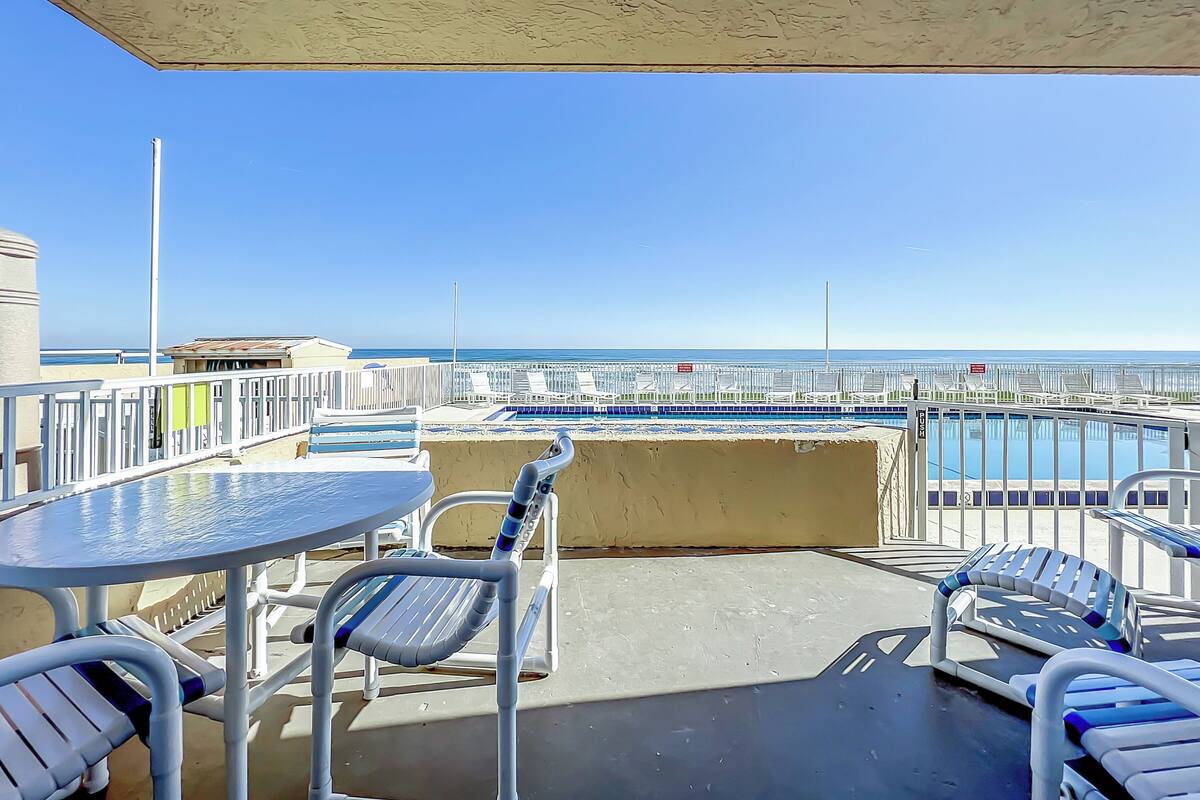 Een balkon met een pooltafel, lounge stoelen en uitzicht op de oceaan en het zwembad.