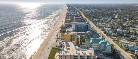 An aerial view of a coastal hotel with a pool, multiple buildings, and a beach.