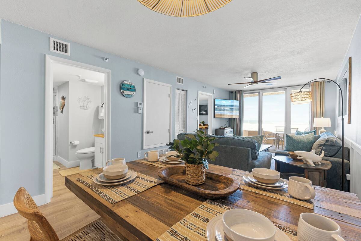 A modern kitchen with a wooden dining table, a built-in oven, and a large window providing natural light.