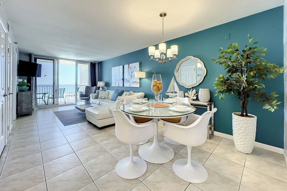 Een moderne eethoek met een glazen tafel, witte stoelen en een wand in zachte blauwgroene tint.
