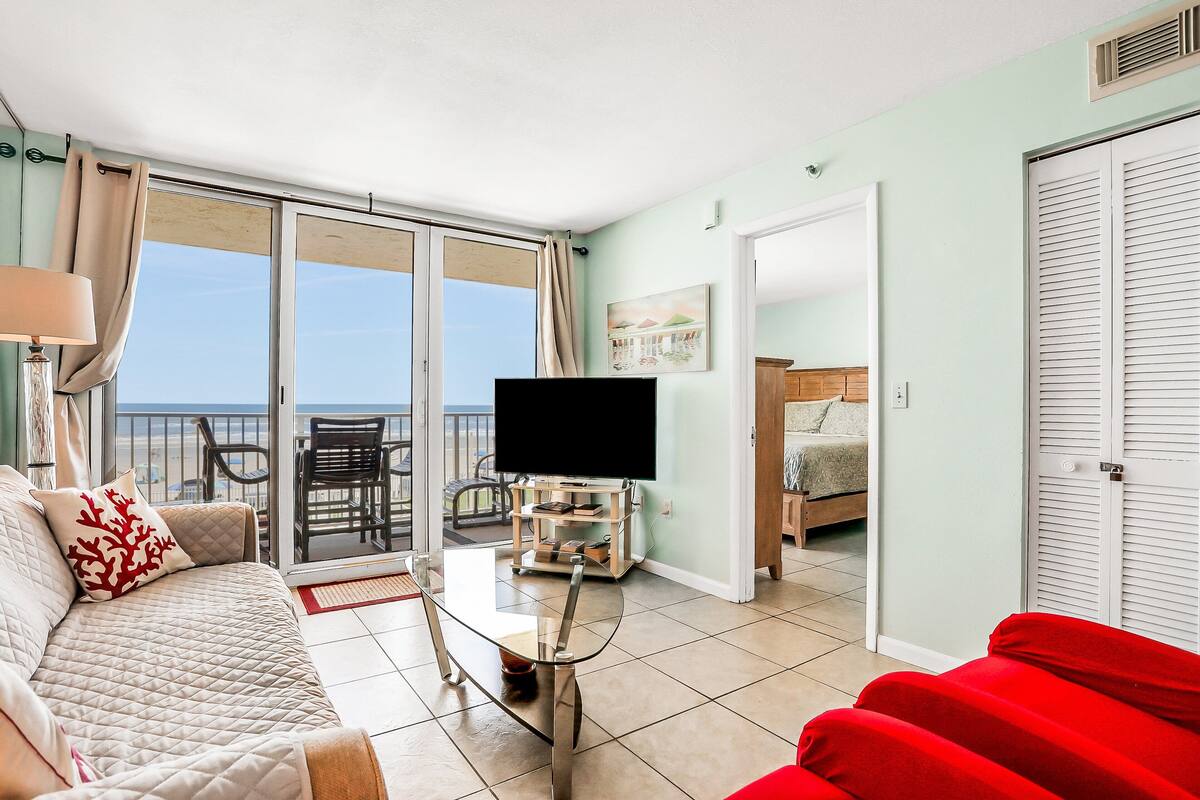 Un salon avec un canapé, un divan rouge, un téléviseur posé sur un meuble et un balcon avec vue.