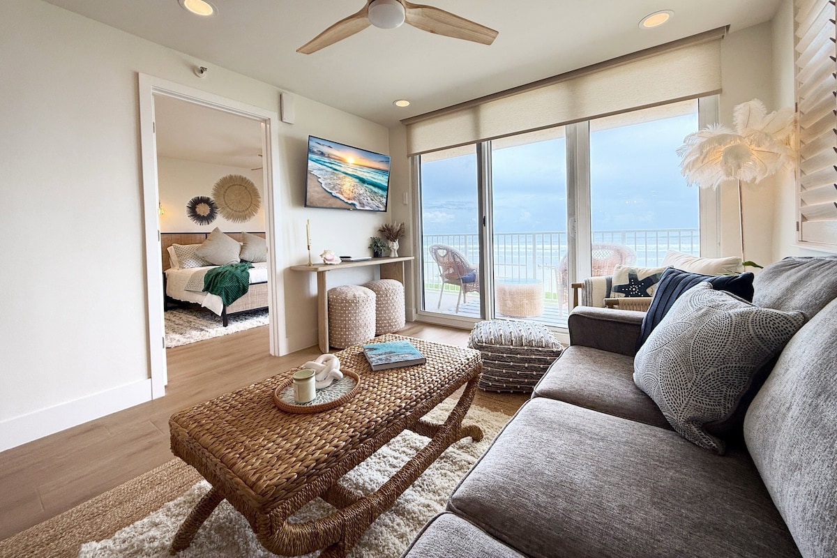 A spacious living room with a large window, a ceiling fan, and a view of the ocean.