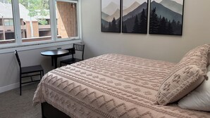A bedroom with a bed, a desk, and a chair. There are three framed pictures on the wall.