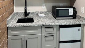 A kitchen with white cabinets, a granite countertop, a black faucet, a microwave, and a small potted plant.