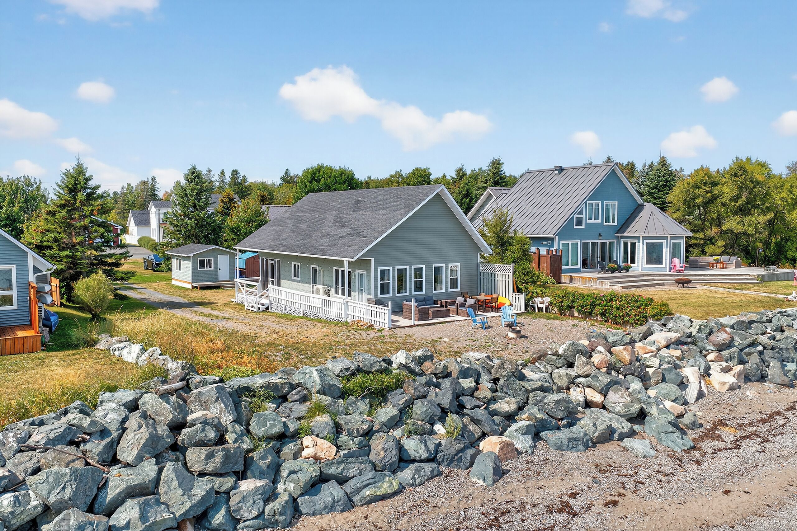 A coastal residential area with houses, a rocky shoreline, and a clear sky.