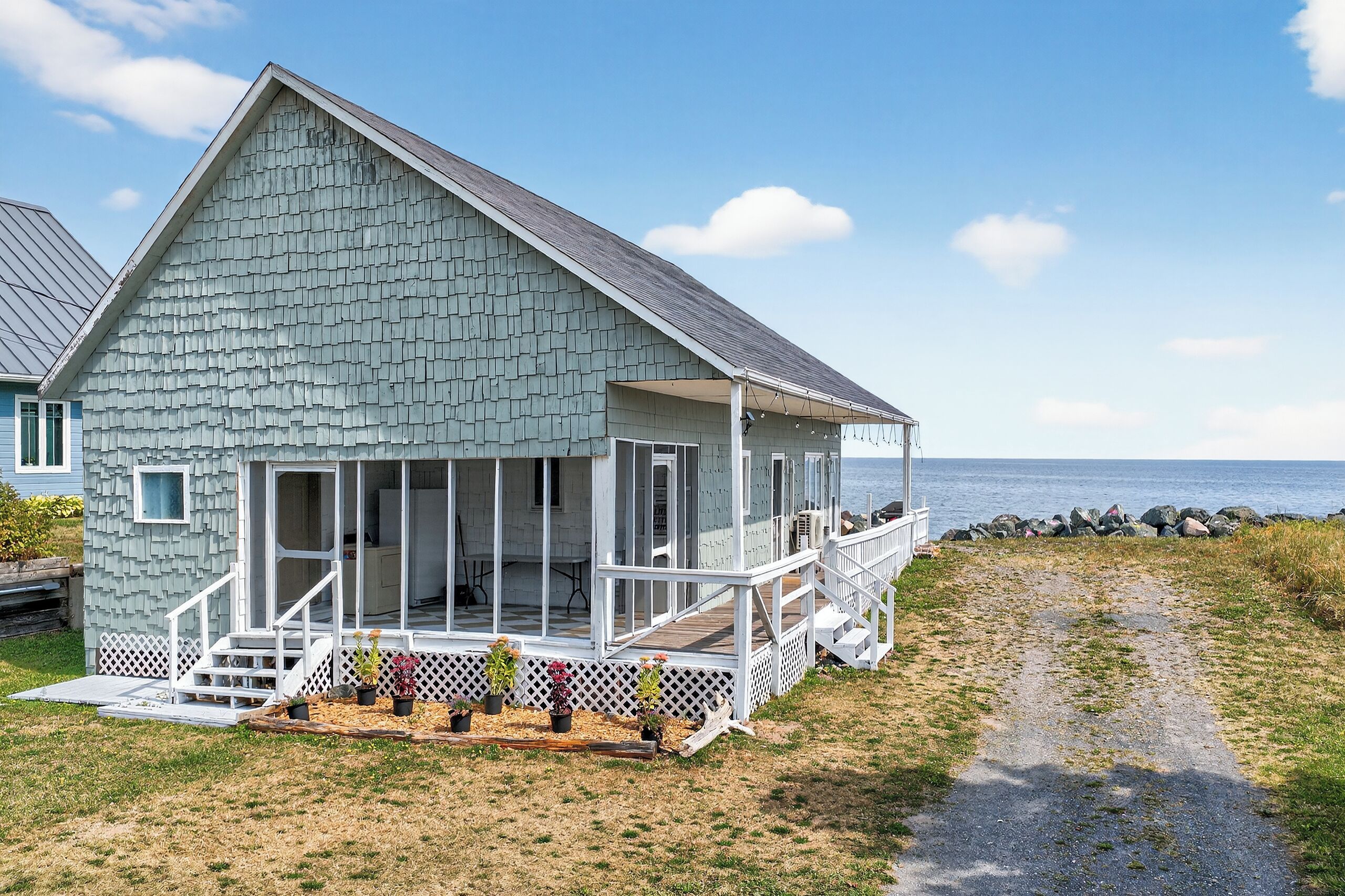 A coastal house with a sloped roof, a porch, and a view of the sea.