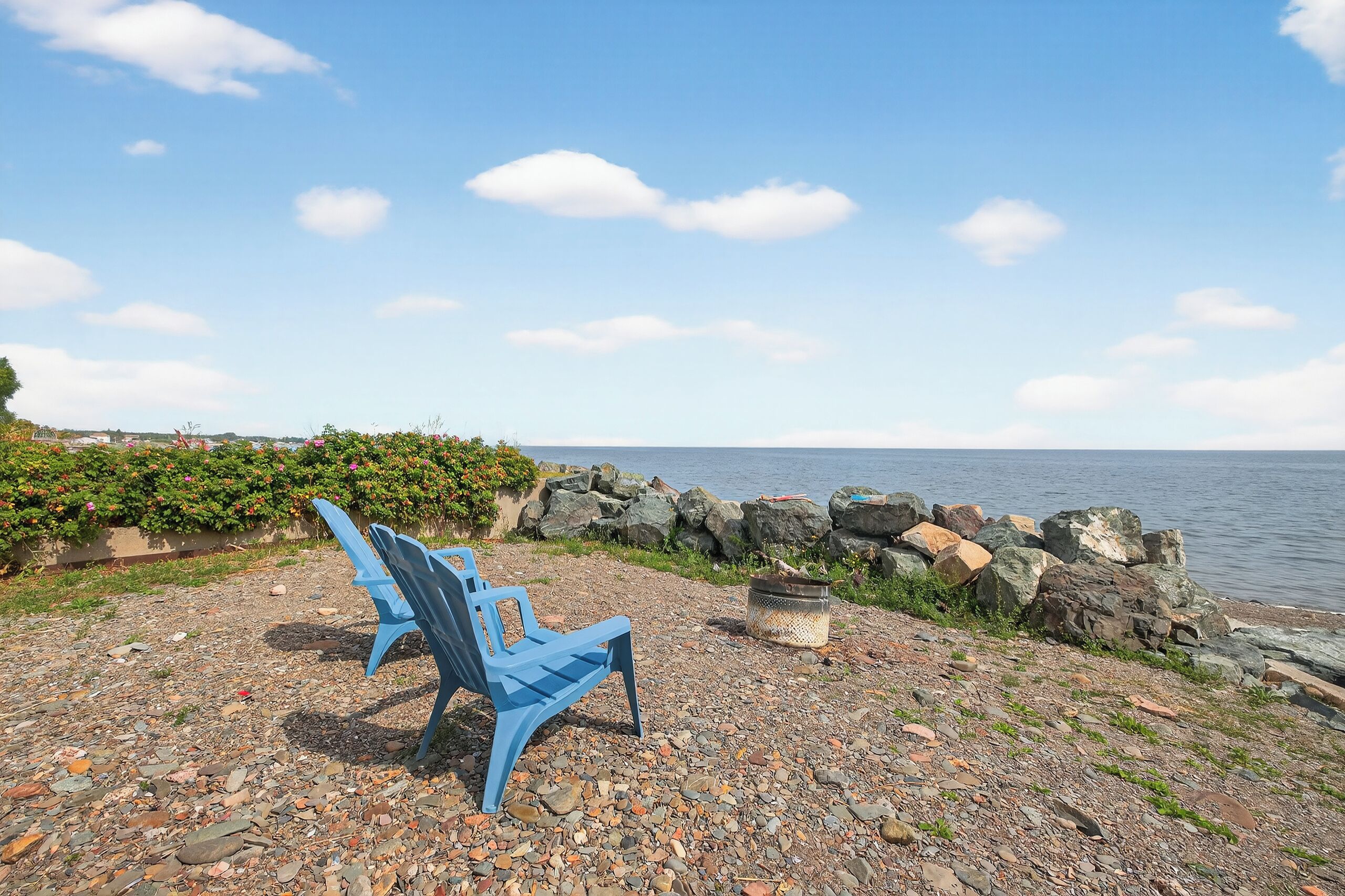A blue chair and a basket on a rocky shore with a view of the sea and a clear sky.