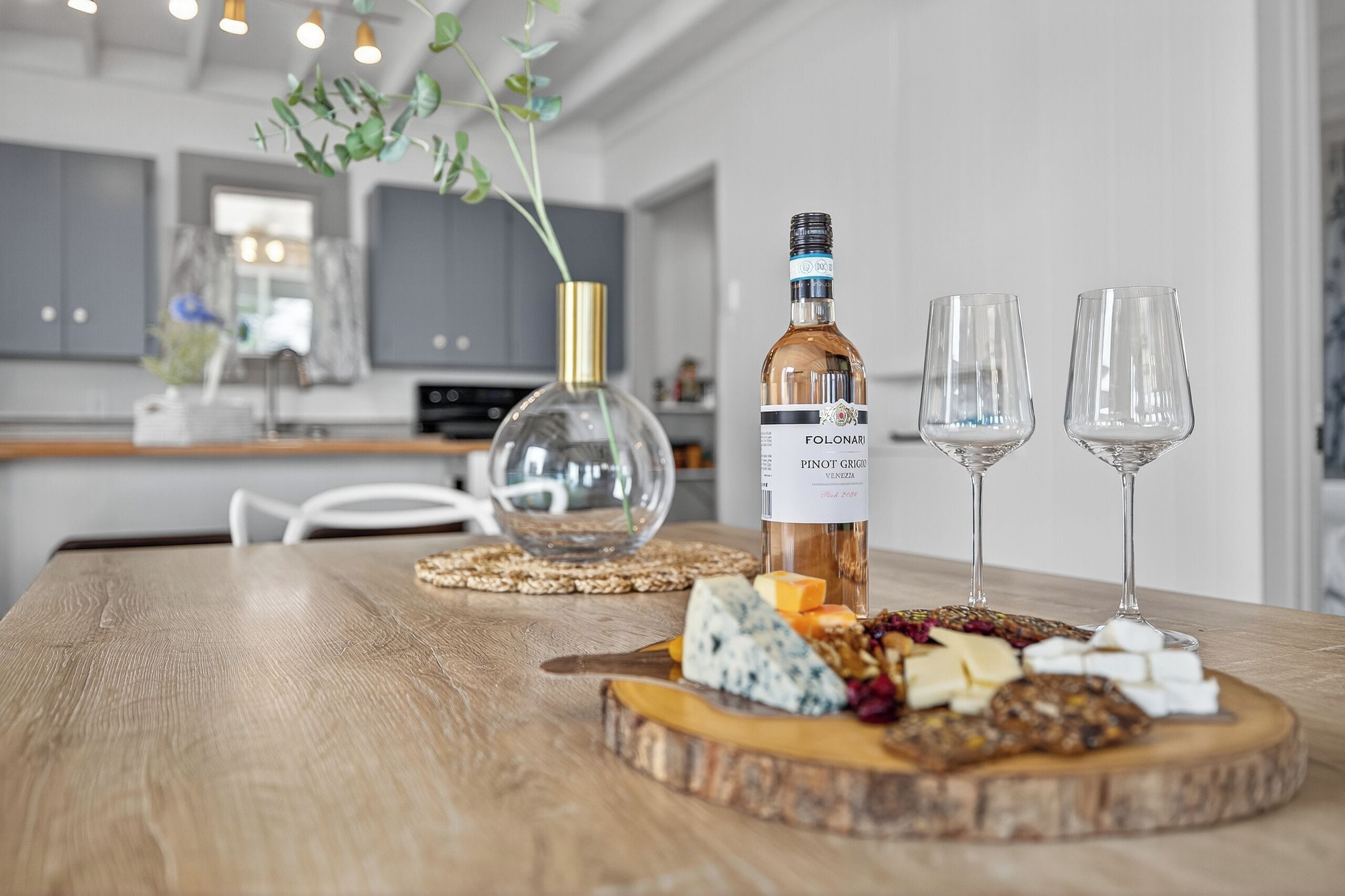 Une table en bois, avec une bouteille de vin, deux verres, et une variété de fromages et de noix.
