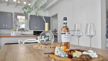Une table en bois, avec une bouteille de vin, deux verres, et une variété de fromages et de noix.