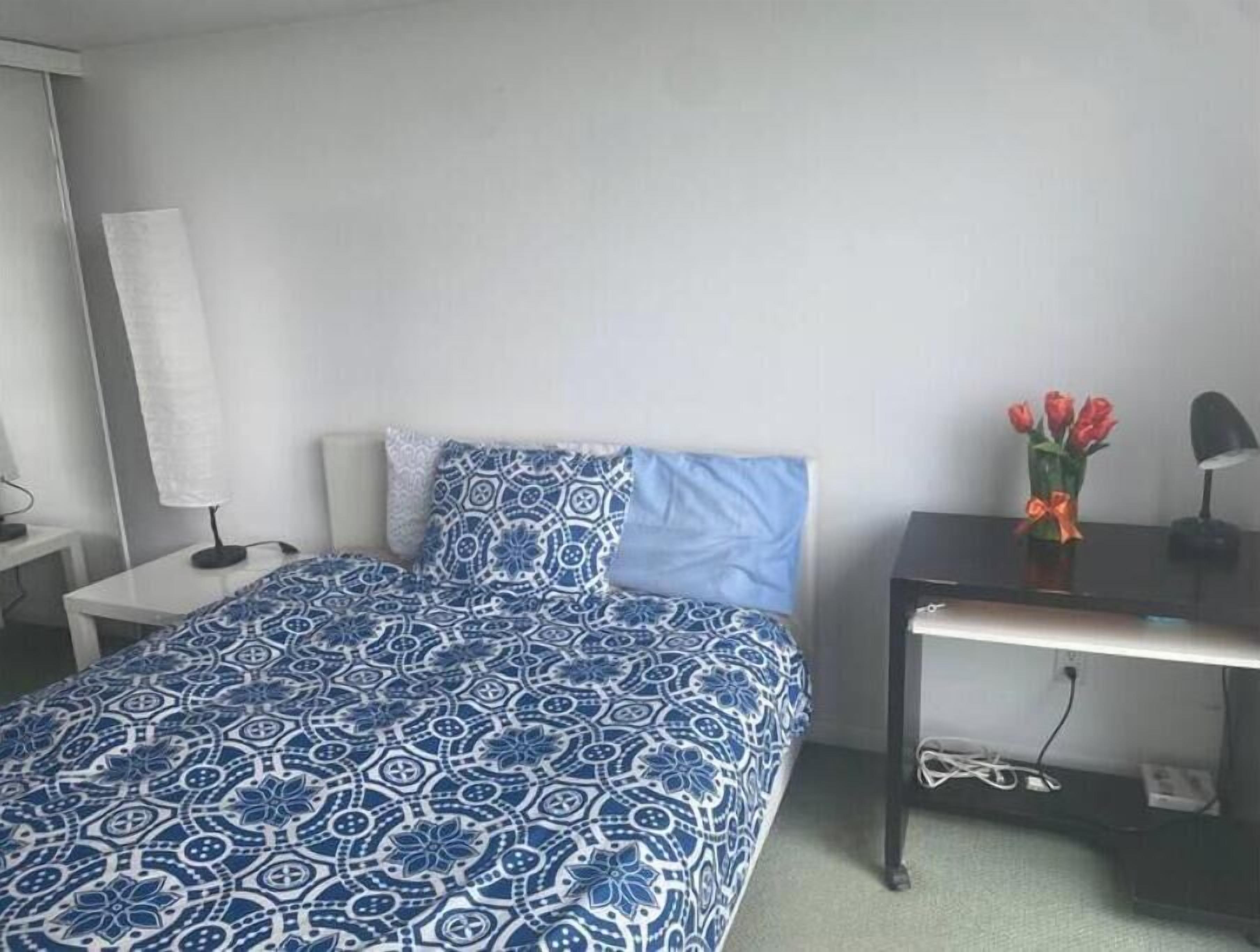 Une chambre à coucher avec un lit, une table de chevet, un bureau et un vase de fleurs.
