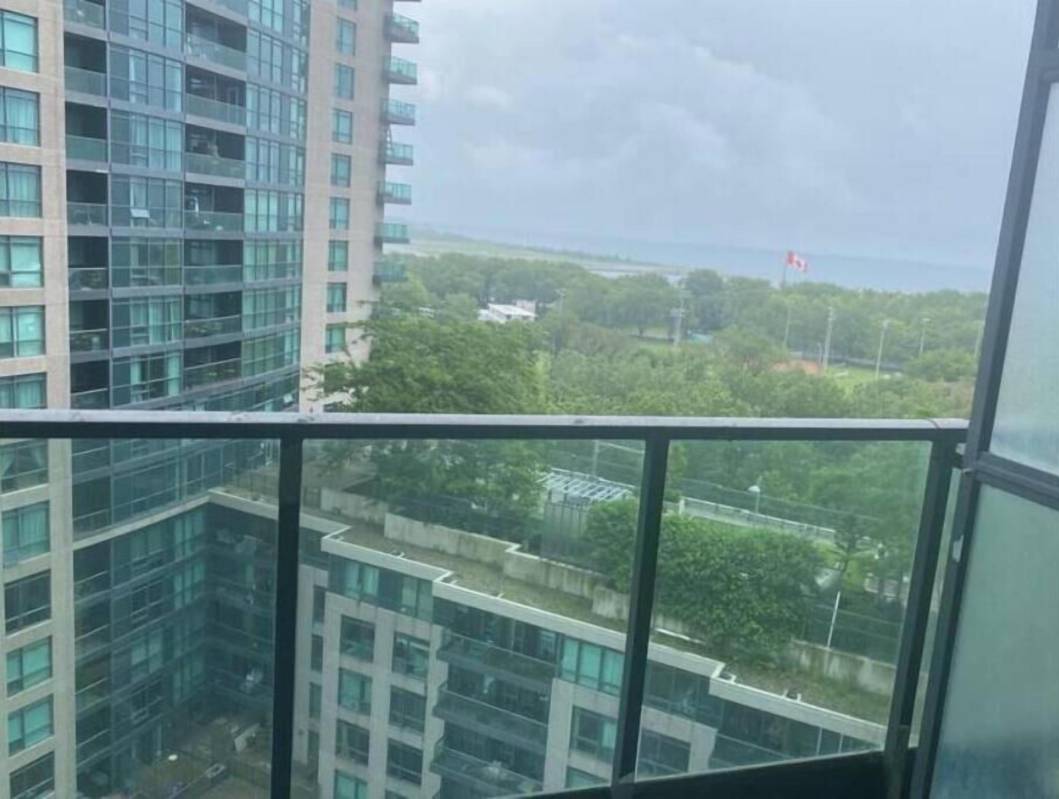 Um edifício alto com vários andares, grandes janelas e vista para áreas verdes e um ponto de referência distante.