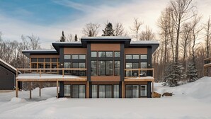 Un edificio moderno de varios pisos con un balcón, rodeado de nieve y árboles.