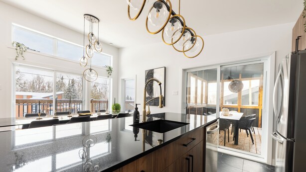 Una cocina moderna con una isla grande, encimeras negras, armarios de madera y un refrigerador de acero inoxidable.