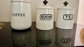 Three white ceramic containers labeled 'Coffee', 'Sugar', and 'Tea' on a reflective surface.