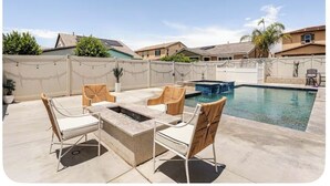 A backyard with a pool, outdoor seating, and a fire pit.