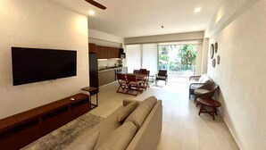 Een moderne woonkamer met een flatscreen televisie, een bank en een eethoek met stoelen.