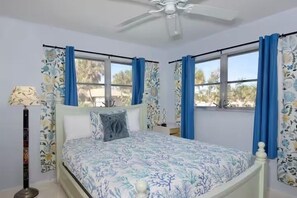 Ein Schlafzimmer mit einem Bett, Deckenventilator und fensterbelaubten Fenstern.