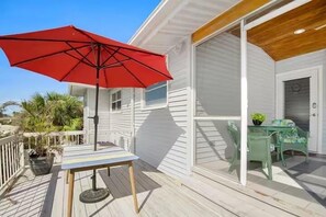 Eine Holzterrasse mit einem roten Sonnenschirm, einem Tisch und Stühlen.