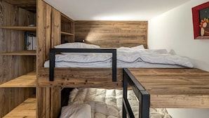 Un lit superposé avec une tête de lit et des étagères en bois, une table de chevet et une œuvre d’art accrochée au mur.