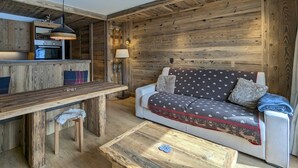 L’intérieur chaleureux d’un chalet avec une table à manger en bois, un canapé agrémenté de coussins à motifs et un coin cuisine doté d’un luminaire suspendu.