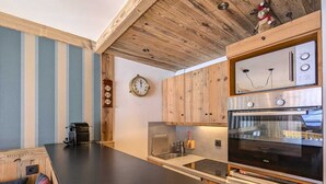 Une cuisine moderne avec des meubles en bois, un plan de travail noir, un four encastré et une horloge au mur.