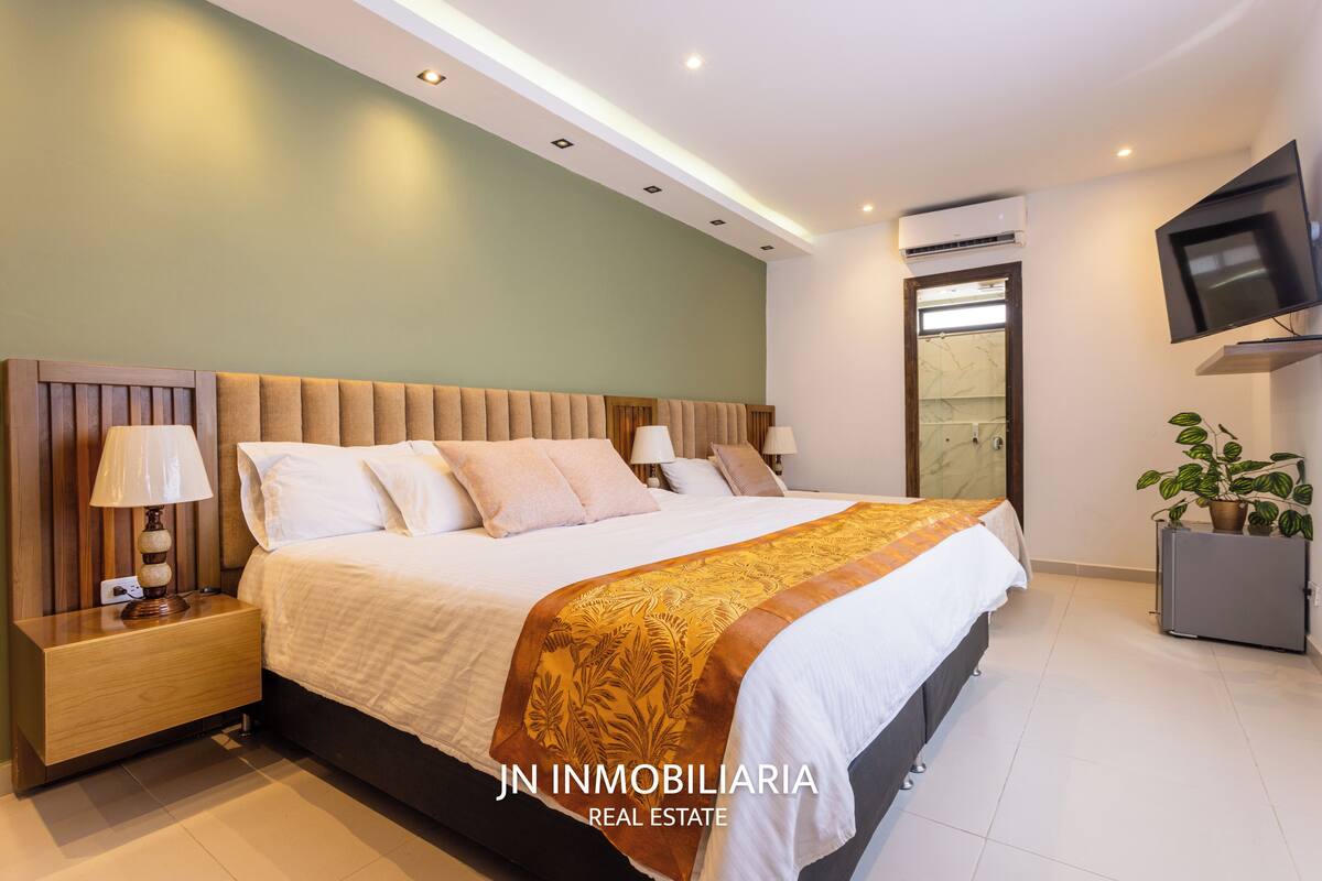 Een moderne slaapkamer met een groot bed, nachtkastjes, een televisie en een airconditioning.