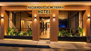 L’extérieur d’un hôtel au design moderne, avec une grande entrée sur laquelle est apposée une enseigne indiquant : « RECUERDOS DE MI TIERRA HOTEL ».