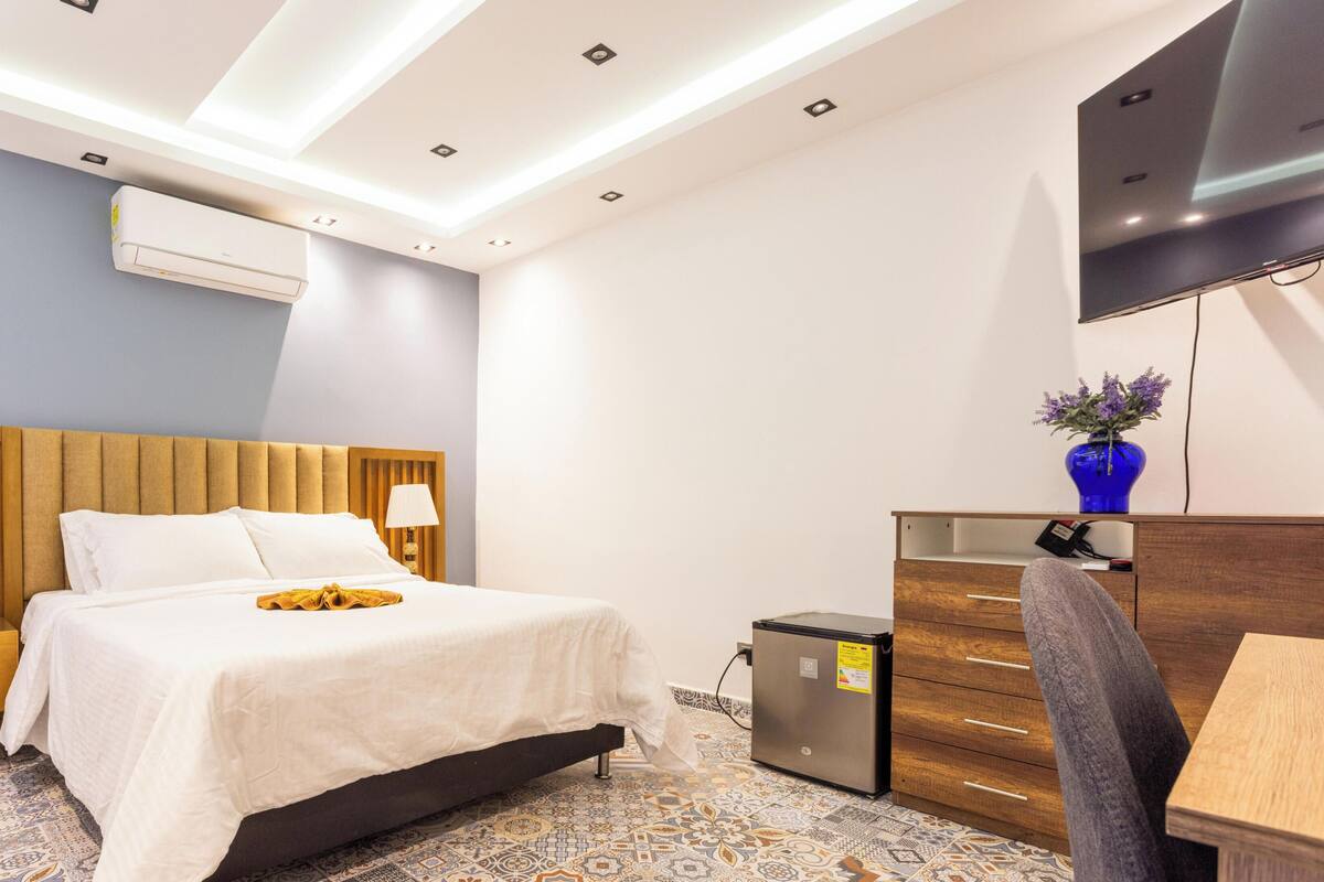 Een moderne hotelkamer met een bed, een bureau, een stoel, een televisie en een airconditioning.