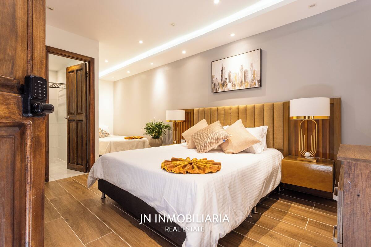 Een moderne hotelkamer met een groot bed, nachtkastjes, een stadsgezicht schilderij en een houten deur met een codeerapparaat.