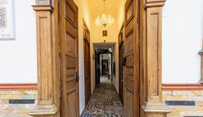 A hallway with wooden doors and a patterned floor, leading to a room with a chandelier. - Recuerdos de mi tierra (Medellin)