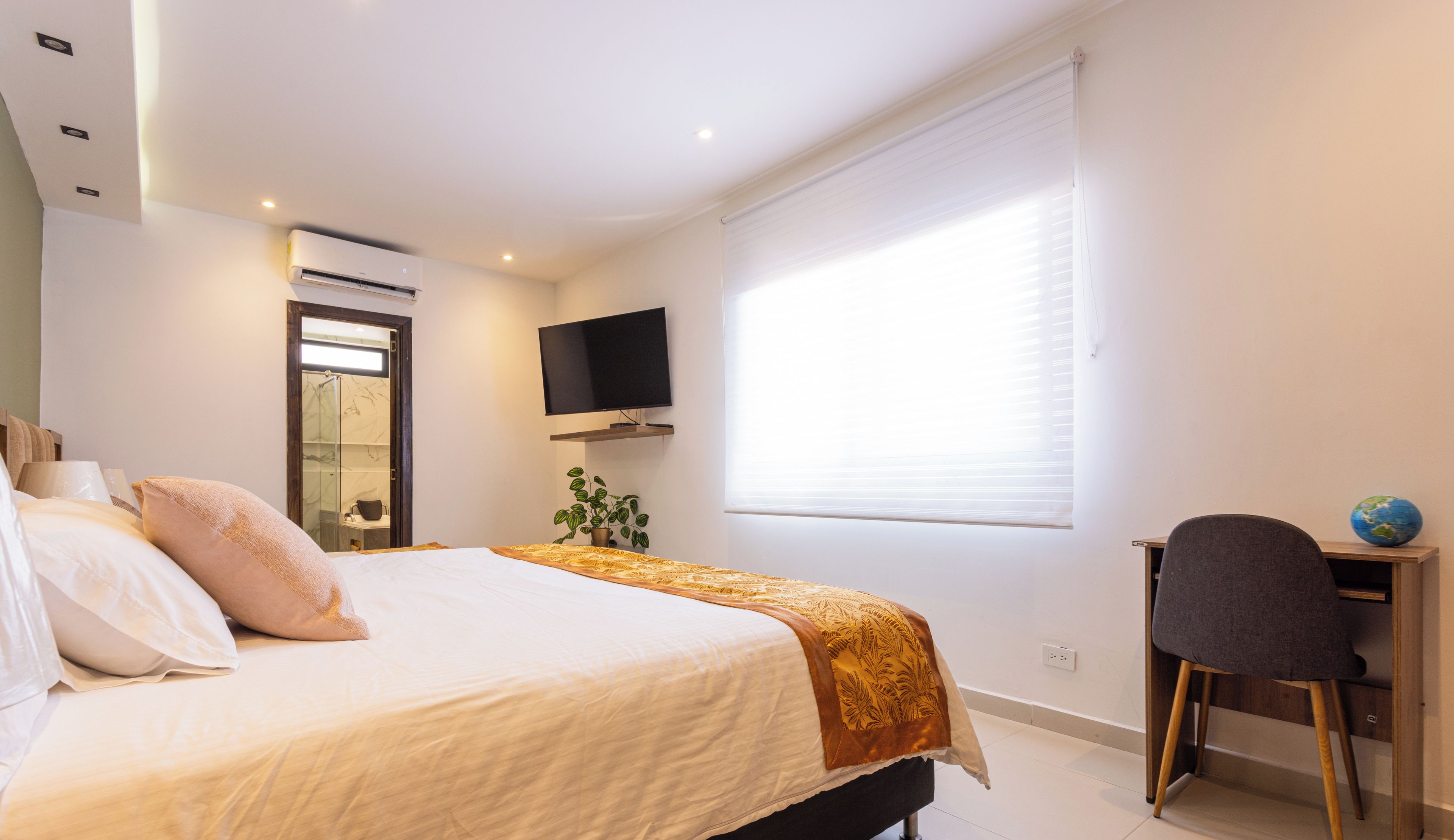 Un dormitorio con cama, escritorio, silla, televisor y ventana.