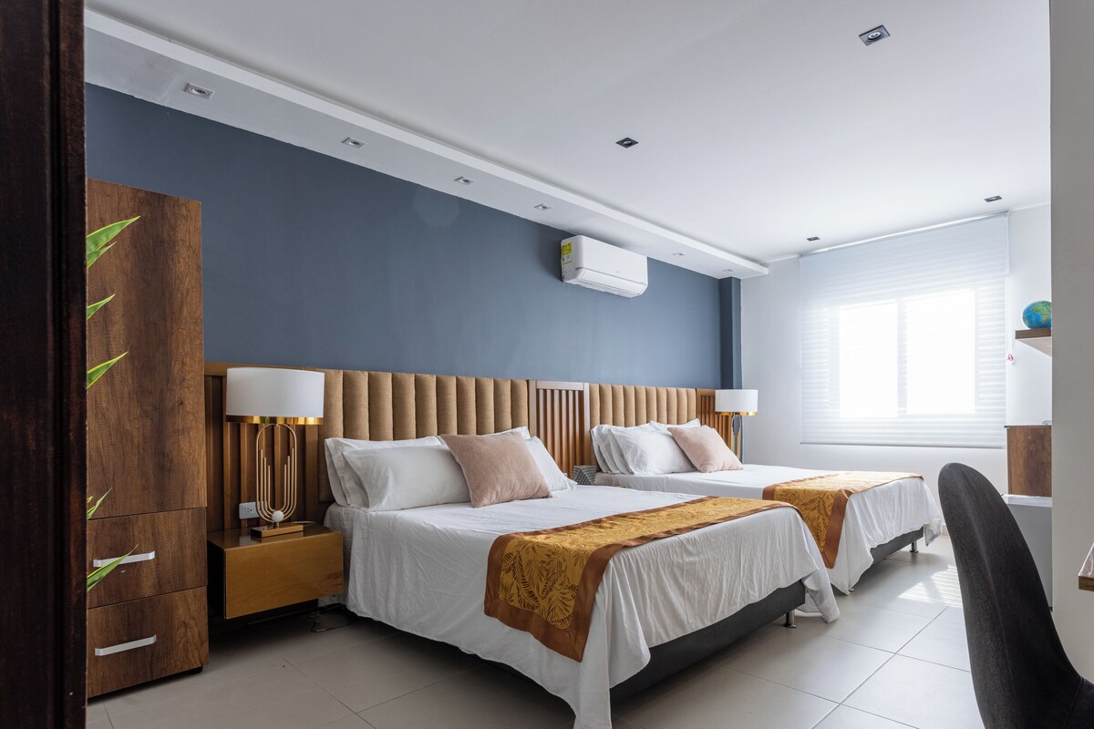 A modern hotel room with two beds, a wooden wardrobe, a desk, and a chair.
