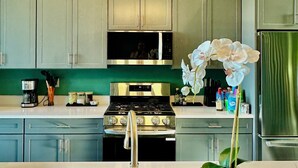 A modern kitchen with a stainless steel stove, a sink with a gold faucet, and a chandelier.