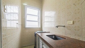 A small kitchen with a sink, window, and patterned walls. - Apto Pet-friendly a 400m da Praia do Boqueir o (Praia Grande)