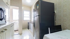 A compact kitchen with a refrigerator, a microwave, and a sink. There is a window providing natural light and a door leading to another room. - Apto Pet-friendly a 400m da Praia do Boqueir o (Praia Grande)