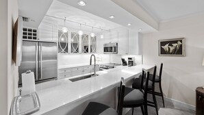 Une cuisine moderne avec des meubles blancs, des appareils en acier inoxydable et des luminaires suspendus.